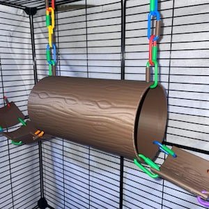 May include: A brown cylindrical tunnel with a textured wood grain pattern, suspended by colorful plastic chains in blue, green, yellow, and red. The tunnel is connected to two smaller curved platforms on either side, all featuring a matching wood grain finish.