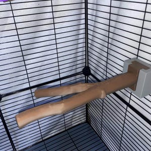 以下が含まれることがあります： ペットケージ用の茶色のY字型枝状パーチ。自然な木を模した滑らかで質感のある表面が特徴です。パーチは、明るい灰色の長方形の取り付けブラケットを使用して、黒いワイヤーケージの壁にしっかりと固定されています。