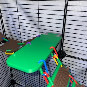May include: A green plastic platform attached to a black wire cage, featuring purple, blue, red, and yellow plastic connectors. A brown textured ramp is suspended from the platform by red and yellow plastic links, with a brown hammock nearby.