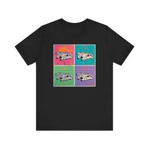 Puede incluir: Camiseta negra con un diseño de estilo pop art de la nave espacial Halcón Milenario. El diseño está dividido en cuatro cuadrados con diferentes fondos de color: rosa, verde azulado, verde y morado. La nave espacial está representada en tonos grises.