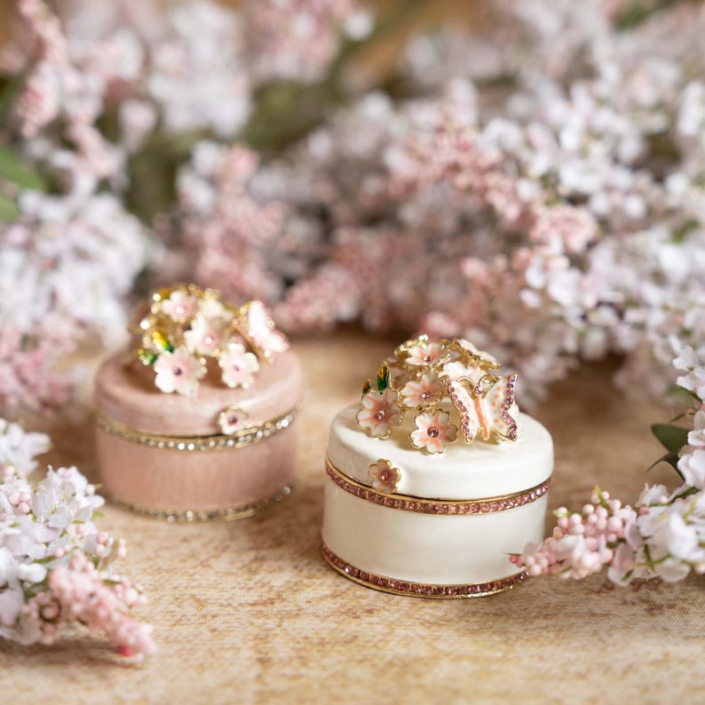 Puede incluir: Dos peque&ntilde;as cajas decorativas con dise&ntilde;os florales rosas y blancos y detalles de mariposas. Las cajas son de cer&aacute;mica y tienen un acabado brillante.