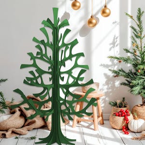 K&ouml;nnte beinhalten: Ein gr&uuml;ner, moderner Weihnachtsbaum aus ausgeschnittenem Holz steht vor einer wei&szlig;en Wand. Goldene Kugeln h&auml;ngen von der Decke. Ein kleiner Weihnachtsbaum und andere Weihnachtsdekorationen befinden sich im Hintergrund. Der Baum ist ein einzigartiges, modernes Design.