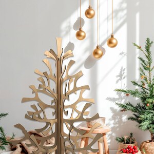 K&ouml;nnte beinhalten: Ein dekorativer Weihnachtsbaum aus Holz mit offenem Design steht vor einer wei&szlig;en Wand. Goldene Kugeln h&auml;ngen von der Decke. Ein kleiner Weihnachtsbaum und andere festliche Dekorationen befinden sich im Hintergrund.