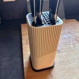 Peut inclure: Un bloc à couteaux rectangulaire avec un extérieur blanc nervuré et une base noire. L'insert supérieur est noir avec un motif géométrique en zigzag, contenant trois couteaux de cuisine à manches noirs et mitres argentées.