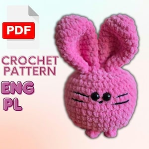 May include: A pink crocheted bunny amigurumi toy with black eyes and whiskers. The toy has long ears and small feet. The image includes the text "CROCHET PATTERN ENG PL" and a PDF icon.
