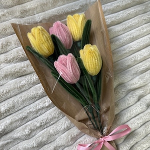 May include: A bouquet of handmade tulips in shades of yellow and pink, wrapped in brown paper and tied with a pink ribbon. The flowers have green stems and leaves, creating a vibrant and cheerful arrangement.
