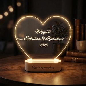 Op de afbeelding: Een hartvormige LED-lamp met de tekst "May 20 Sebastian Valentina 2026" en "You're my everything" gegraveerd op een houten voet. De lamp straalt een warme, zachte gloed uit, perfect voor een nachtkastje of bureau.