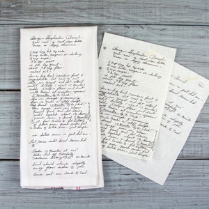 May include: A white kitchen towel with handwritten recipe notes, alongside two loose recipe cards. The towel has red stripes at the bottom. The recipe appears to be for a type of bread.