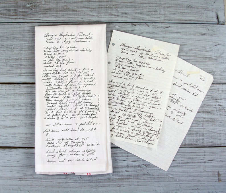 May include: A white kitchen towel with handwritten recipe notes, alongside two loose recipe cards. The towel has red stripes at the bottom. The recipe appears to be for a type of bread.