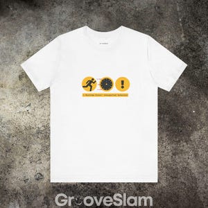 Op de afbeelding: Wit T-shirt met een gele rennende figuur, een klok en een uitroepteken. De tekst "Runtime Error: Unexpected behavior" is onder de afbeelding gedrukt.