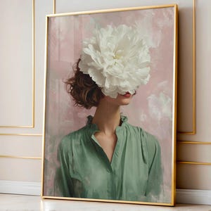 Peut inclure: Impression artistique encadrée représentant une femme avec une grande fleur blanche cachant son visage. Elle porte une blouse verte sur un fond abstrait rose et blanc. L'œuvre est encadrée dans un cadre doré.