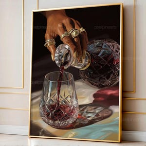 Può includere: Una stampa artistica incorniciata raffigura una mano che versa vino rosso in un bicchiere di cristallo. La mano, ornata di anelli d'oro e unghie smaltate, tiene una caraffa di vetro. Il bicchiere da vino e la caraffa hanno un motivo a diamante. Lo sfondo è scuro.