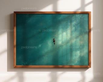 May include: A framed art print featuring a person swimming in turquoise water. The artwork is set in a wooden frame and is mounted on a white wall. The image is lit by sunlight, creating shadows.