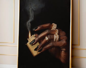 May include: A framed artwork depicts a hand holding a gold lighter with a flame and smoke against a black background. The hand is adorned with multiple gold rings with clear stones and black nail polish.