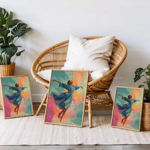 May include: Three framed art prints featuring a dancer in a flowing blue dress against a colorful abstract background of pink, orange, and green. The prints are displayed in a room with a wicker chair and plants.