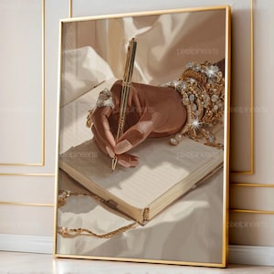 以下が含まれることがあります： 金色のペンでノートに書いている手のフレームアートプリント。手には金の指輪とブレスレットが飾られています。アートワークは、金のアクセントを持つニュートラルなカラーパレットです。