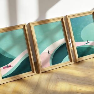 Pode incluir: Três impressões de arte emolduradas com paisagens abstratas com figuras. Cada impressão tem uma moldura de madeira clara e retrata uma pessoa em um caminho rosa contra um fundo verde e turquesa. A obra de arte é exibida em um piso de madeira.