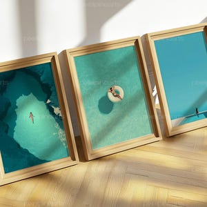 Könnte beinhalten: Drei gerahmte Kunstdrucke mit ruhigen Wasserszenen. Einer zeigt eine Person, die in einer türkisfarbenen Höhle schwimmt, ein anderer eine Person auf einem Pool-Schwimmring und der letzte eine Person auf einem Pooldeck. Die Rahmen sind aus hellem Holz.
