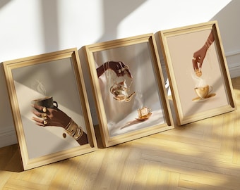 May include: Set of three framed art prints featuring illustrations of hands adorned with gold jewelry. One print shows a hand holding a cup of coffee, another pouring tea, and the third adding a cookie to a teacup. The prints have a warm, neutral color palette.