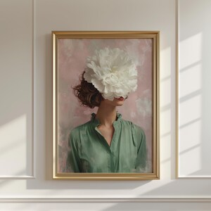 以下が含まれることがあります： 大きな白い花で顔を覆った女性が描かれた、額入りのアートプリント。彼女はピンクと白の背景に、緑色のブラウスを着ています。アートワークは金色のフレームに入っており、ヴィンテージな美しさを醸し出しています。