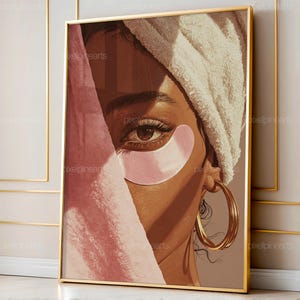 May include: A framed art print featuring a woman with brown skin, wearing a white towel on her head and pink under-eye patches. The woman's eye is visible, with long eyelashes and a gold hoop earring. The artwork has a warm, inviting color palette.