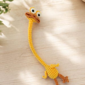 Peut inclure: Une girafe au crochet jaune faite à la main, avec un long cou, de petites ailes et des pieds marron. La girafe a de grands yeux globuleux et un bec marron. Le jouet est fait de fil doux et est probablement un jouet pour enfant ou un objet décoratif.