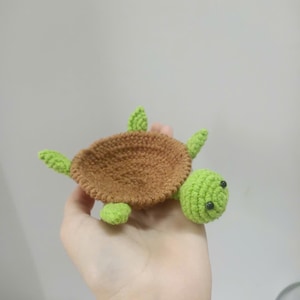 Op de afbeelding: Een handgemaakte gehaakte schildpad met een bruin schild en groene kop, vinnen en accenten. De schildpad heeft kleine zwarte ogen. Dit zachte speelgoed is een schattig, grillig item.