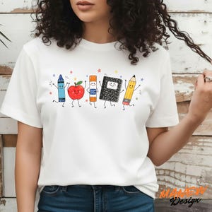 May include: A white t-shirt featuring a graphic print of five animated school supplies: a blue crayon, a red apple, an orange glue stick, a black and white composition notebook, and a yellow pencil, all with smiling faces and thin limbs.