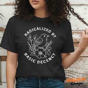May include: Black t-shirt with a white graphic of a bird perched on flowers, surrounded by the words "RADICALIZED BY BASIC DECENCY". The design is centered on the shirt.