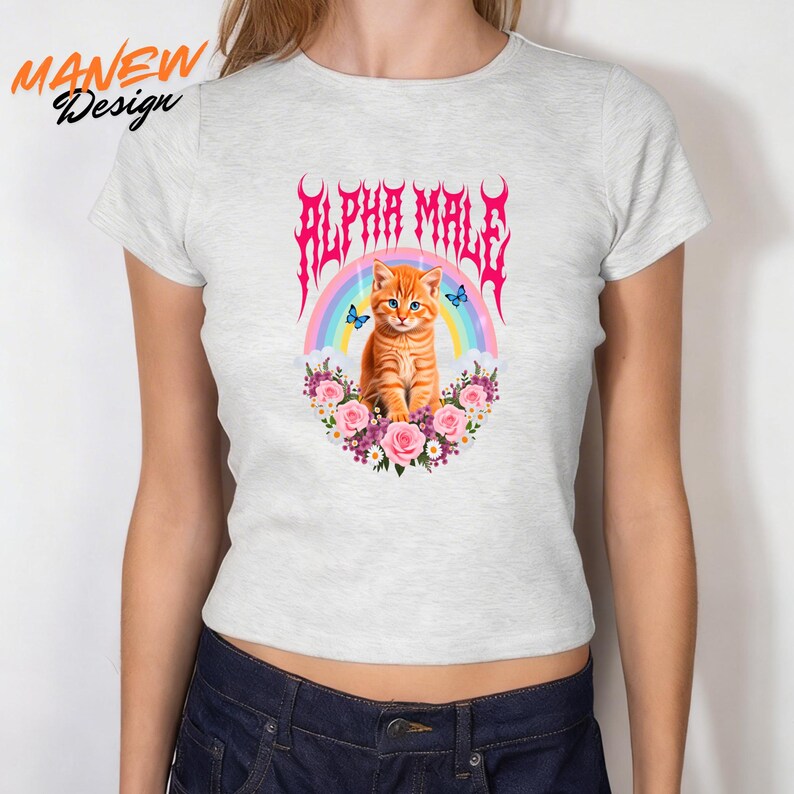 Pode incluir: Camiseta cinza claro com um gr&aacute;fico de um gato malhado laranja com olhos azuis, um arco-&iacute;ris e o texto "ALPHA MALE" em rosa. O gato &eacute; cercado por flores rosa e roxas e borboletas azuis.