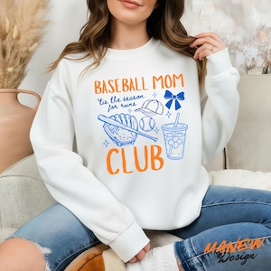 Op de afbeelding: Witte sweatshirt met een oranje en blauwe baseball-afbeelding. Het ontwerp bevat de woorden "Baseball Mom Club" en de zin "'Tis the season for runs", samen met honkbalillustraties zoals een knuppel, bal en handschoen.
