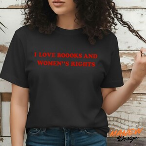 May include: A black short-sleeved t-shirt featuring the red text I LOVE BOOOKS AND WOMEN'S RIGHTS printed across the chest. The garment has a crew neckline and a standard fit, showcasing bold lettering in a simple, clean font style on the front.