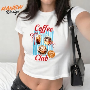Op de afbeelding: Witte crop top met een "Coffee Club" ontwerp. Het ontwerp bevat illustraties van koffiedranken, waaronder ijskoffie, een cappuccino en een latte met een hartvormig ontwerp. De woorden "all day every day" zijn ook opgenomen.