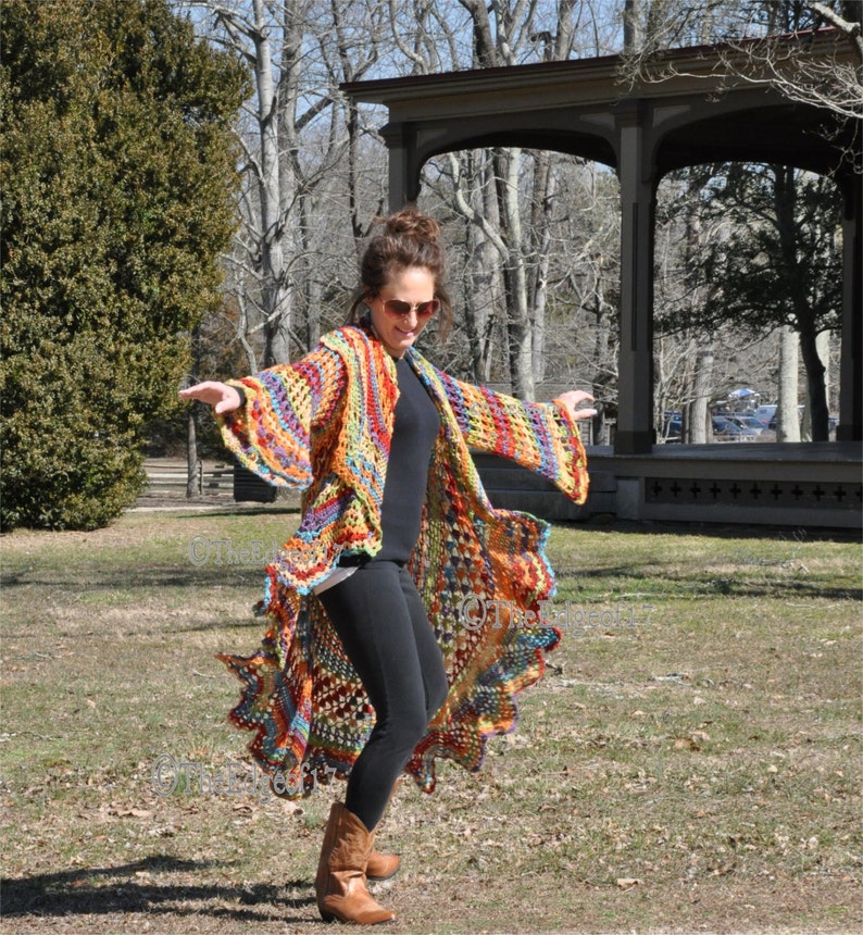 May include: A colourful, handmade crochet cardigan with long sleeves and an asymmetrical hemline. The open-front design displays a mix of orange, yellow, blue, and green hues. The garment's bohemian style is evident in its intricate crochet pattern.