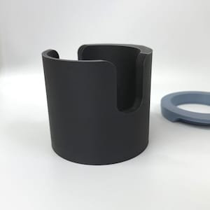 Puede incluir: Un soporte cil&iacute;ndrico negro con una abertura curva y un anillo azul separado. El objeto cil&iacute;ndrico parece ser un soporte. Los objetos est&aacute;n sobre un fondo blanco.