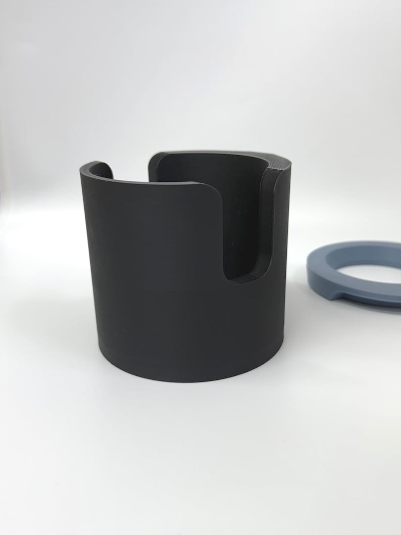 Puede incluir: Un soporte cil&iacute;ndrico negro con una abertura curva y un anillo azul separado. El objeto cil&iacute;ndrico parece ser un soporte. Los objetos est&aacute;n sobre un fondo blanco.