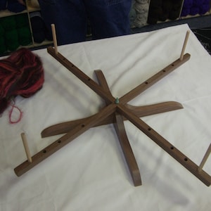 May include: A wooden yarn swift with five spindles, each with a wooden dowel. The swift is made of dark wood and has a natural finish. The swift is sitting on a white surface.