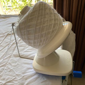 以下が含まれることがあります： 白い糸玉が、青いクランクが付いた白い糸巻きに載っています。糸巻きは白い表面の上に置かれています。