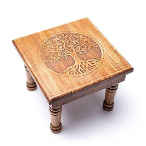Peut inclure: Petite table carrée en bois clair avec un motif d'arbre de vie sculpté sur le dessus. Elle repose sur quatre pieds tournés. La sculpture de l'arbre est d'une teinte plus claire.