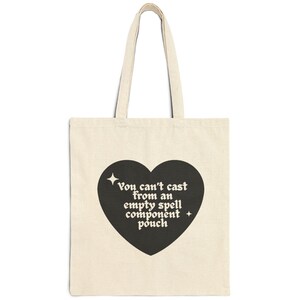 Könnte beinhalten: Eine beige Canvas-Tragetasche mit schwarzen Henkeln und einer schwarzen herzförmigen Grafik. Die Grafik zeigt den Text "You can't cast from an empty spell component pouch" in einer Retro-Schrift.