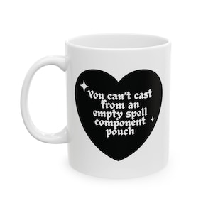 Könnte beinhalten: Weiße Keramiktasse mit einem schwarzen Herzdesign. Das Herz enthält den Text "You can't cast from an empty spell component pouch" in einer stilisierten Schriftart. Die Tasse hat einen gebogenen Griff.
