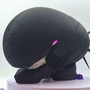 May include: A black, futuristic-looking sculpture with a rounded, helmet-like top and spiky protrusions. The sculpture has a glowing pink light and rests on a purple base. The design is reminiscent of science fiction.