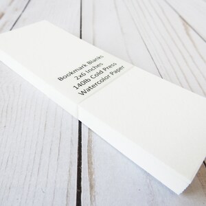 May include: A stack of white bookmark blanks, 2x6 inches, made of 140lb cold press watercolor paper.