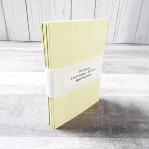 May include: A stack of 60 blank ATC cards in a pale yellow color, with a label that reads "ATC Blanks 2.5x3.5 Inches - 60 Count Aged Parchment".