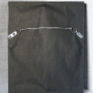 May include: The back of a black framed picture with a white string attached to two metal hooks. The hooks are attached to the frame with screws.