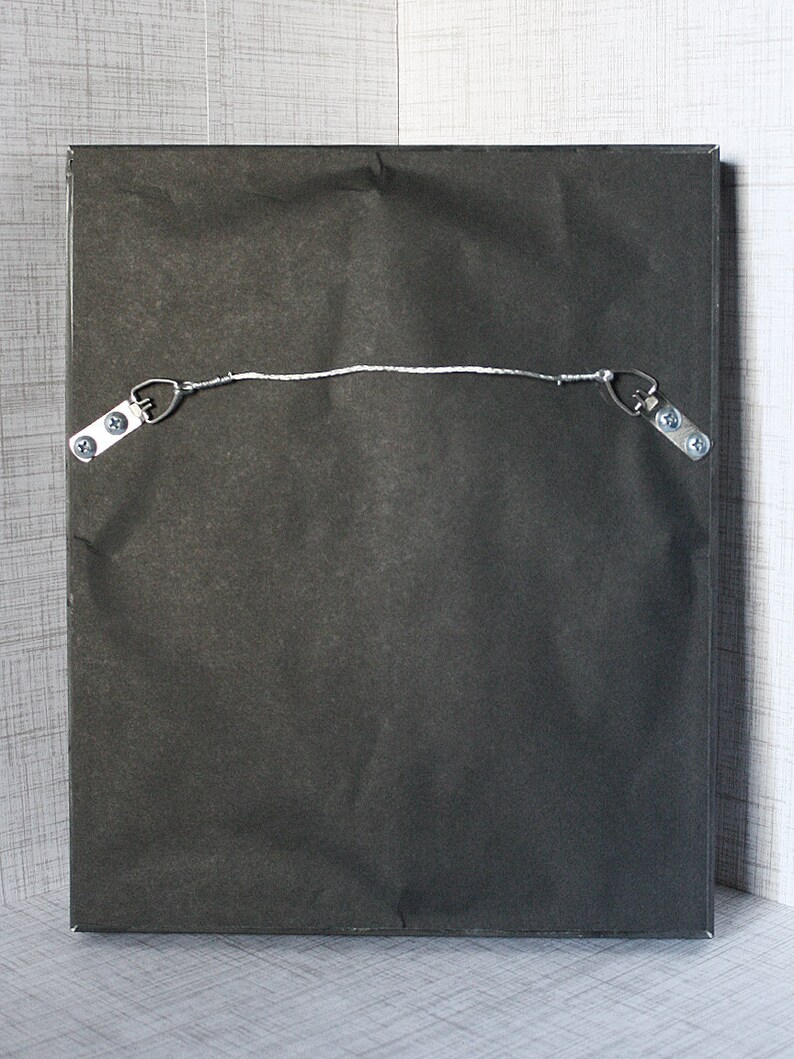May include: The back of a black framed picture with a white string attached to two metal hooks. The hooks are attached to the frame with screws.