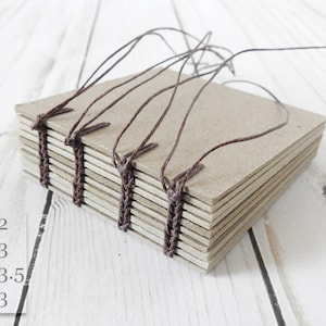 May include: A stack of brown cardboard pages are bound together with brown string. The pages are sewn together with a coptic stitch. The text on the image reads: 2x2, 2x3, 2.5x3.5, 3x3.