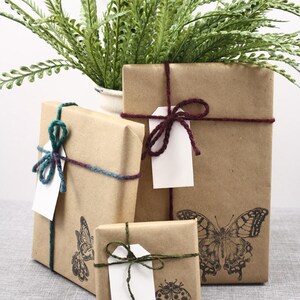 May include: Three brown paper gift boxes wrapped with twine and tied with bows. The boxes are decorated with butterfly and ladybug stamps. The boxes are sitting on a gray textured surface.