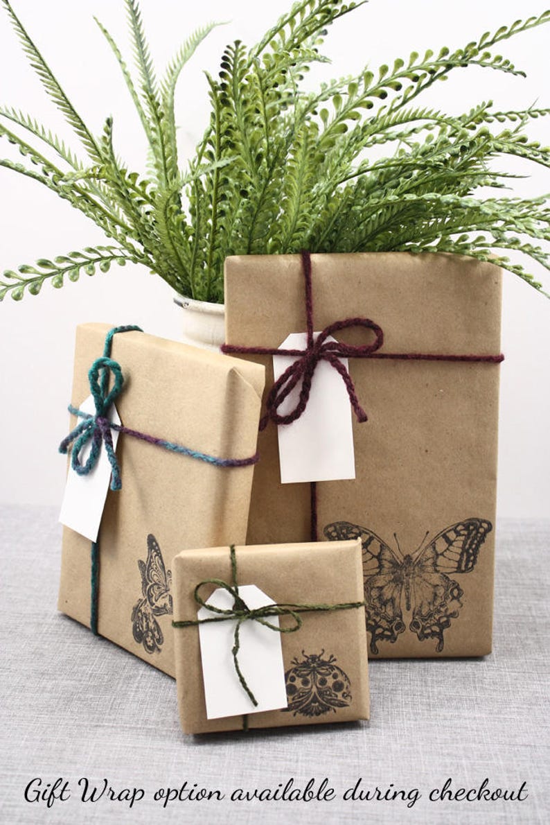 May include: Three brown paper gift boxes wrapped with twine and tied with bows. The boxes are decorated with butterfly and ladybug stamps. The boxes are sitting on a gray textured surface.