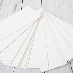 May include: A stack of blank white rectangular cards, fanned out on a white wooden surface.